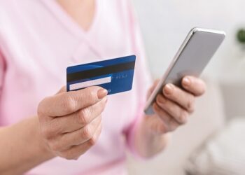 Senior woman shopping online on smartphone, paying with credit card, closeup