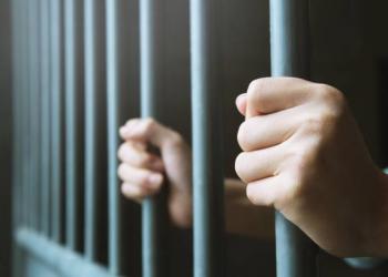 Man in prison hands of behind hold Steel cage jail bars. offender criminal locked in jail.