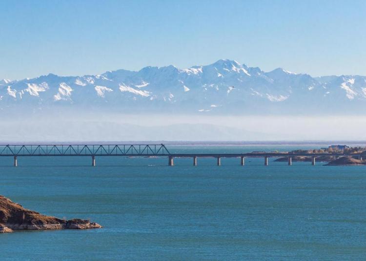 View of the Kapchagay reservoir with islands and a railway bridge against the backdrop of mountains in the Almaty region of Kazakhstan.